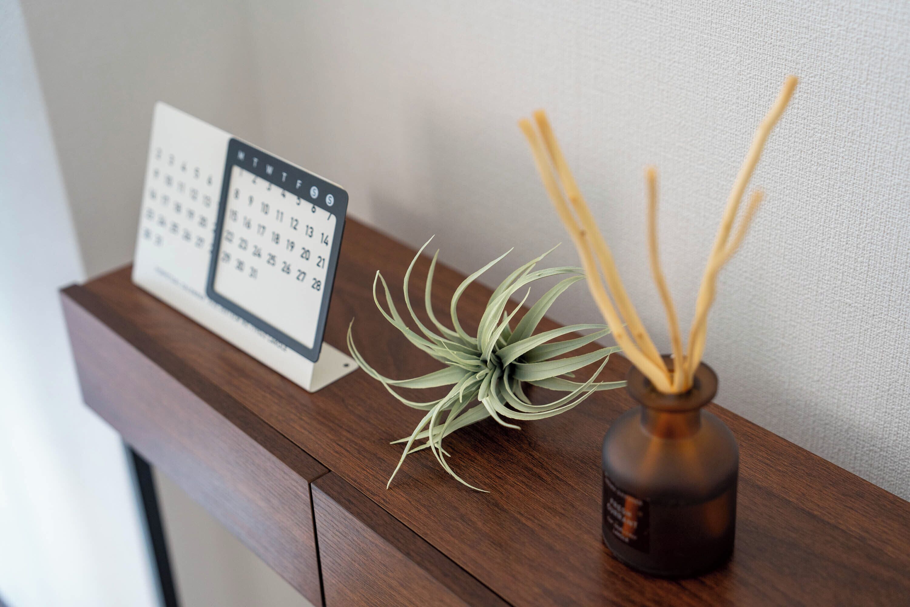 A wooden table with a calendar, a small potted plant, and a reed diffuser.