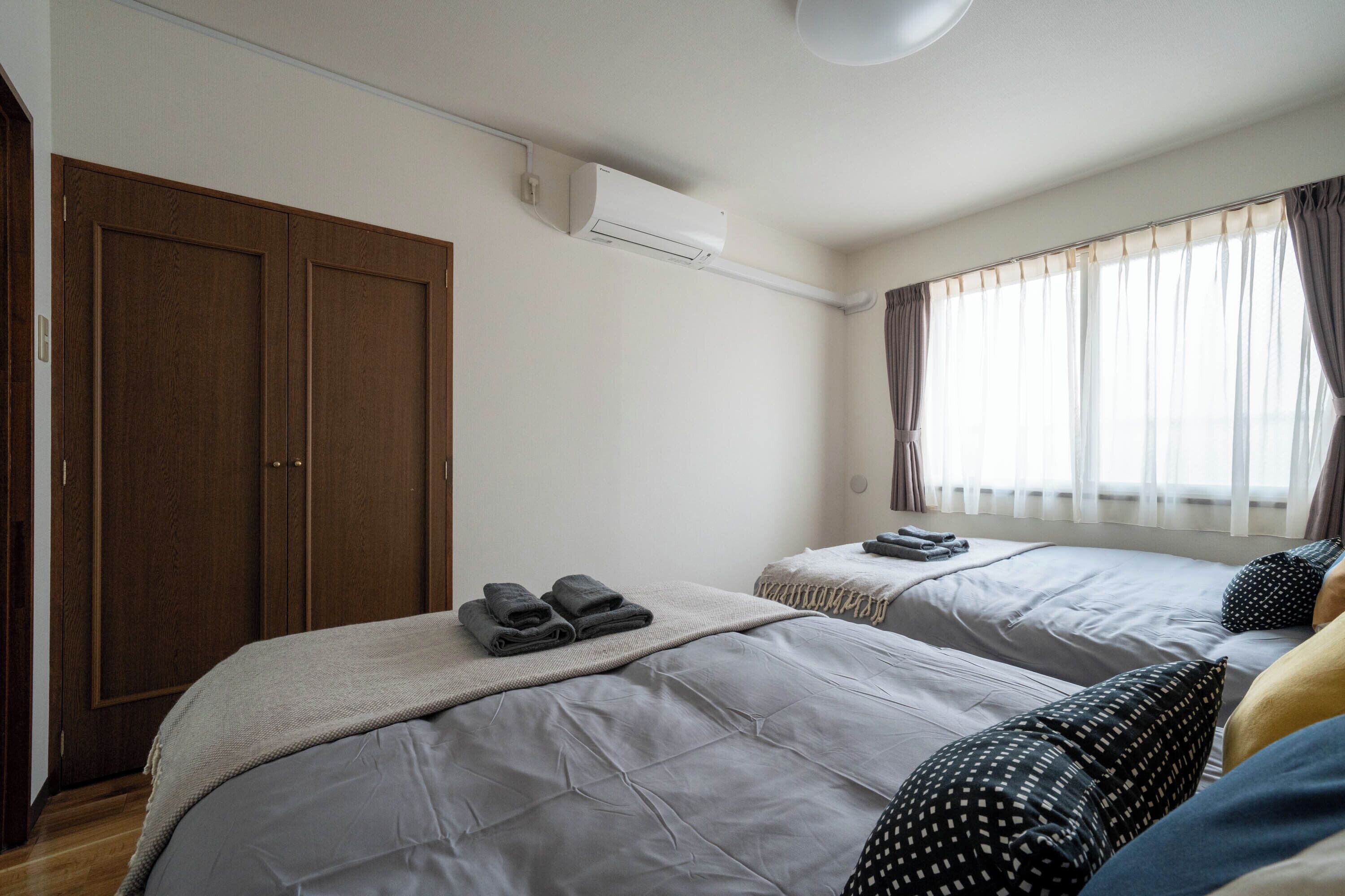 Ein Hotelzimmer mit zwei Betten, einem Kleiderschrank, einer Klimaanlage und einem Fenster mit Vorhängen.