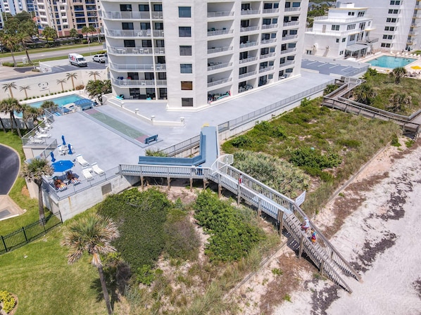 A multi-story hotel with a pool, outdoor seating, and a beach access walkway.
