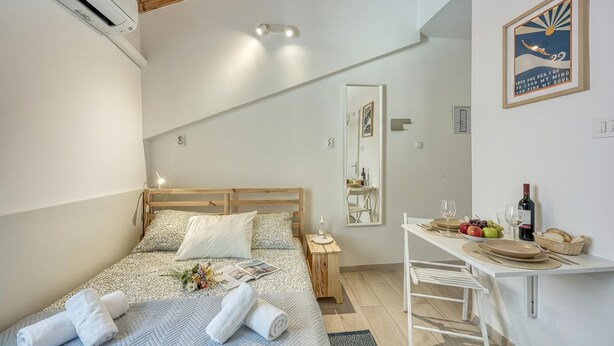 A bedroom with a bed, bedside table, and a small dining area with a table and chairs.
