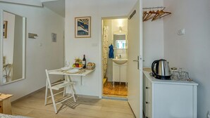 A compact room with a dining table, a small kitchen area, a mirror, and a cabinet with a kettle.