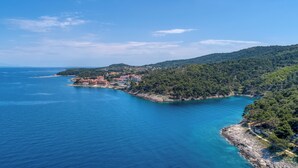 A coastal town with buildings along the shoreline, surrounded by hills and a clear blue sea.