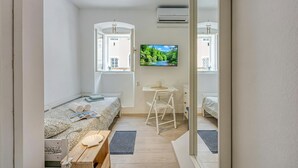 Un dormitorio compacto con cama, un escritorio pequeño, una silla y televisión en la pared.