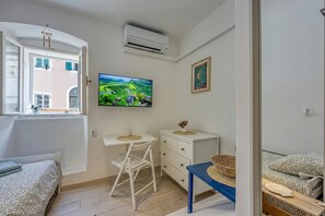 Ein Schlafzimmer mit Bett, Schreibtisch, Stuhl, Fernseher und Fenster.