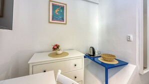 Una habitación pequeña y limpia con un aparador blanco, una mesita auxiliar azul con una cesta, una tetera y un cartel enmarcado en la pared.