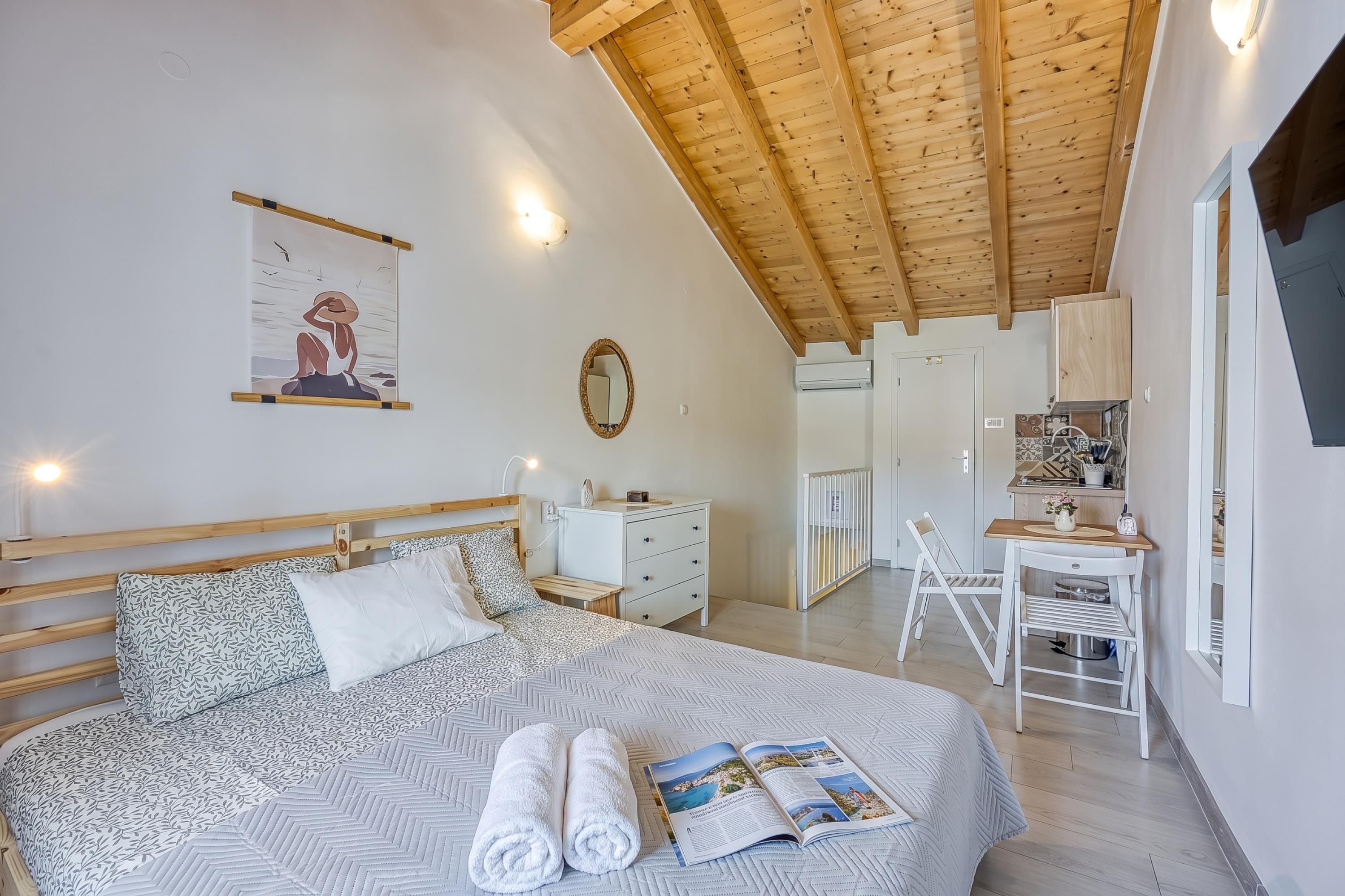 Une chambre à coucher comprenant un lit, des tables de chevet, un miroir et donnant sur la pièce adjacente.