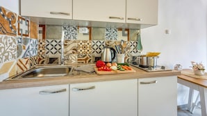 Una cocina con baldosas estampadas, un fregadero, una tabla de cortar con verduras, una tetera y una olla sobre la encimera.