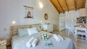 Un dormitorio con techo de madera, cama con ropa de cama estampada, mesita de noche, escritorio pequeño con silla y un espejo colgado en la pared.