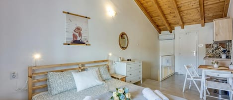 A bedroom with a wooden ceiling, a bed with patterned bedding, a bedside table, a nightstand, a wall-mounted mirror, and a small desk with a chair.