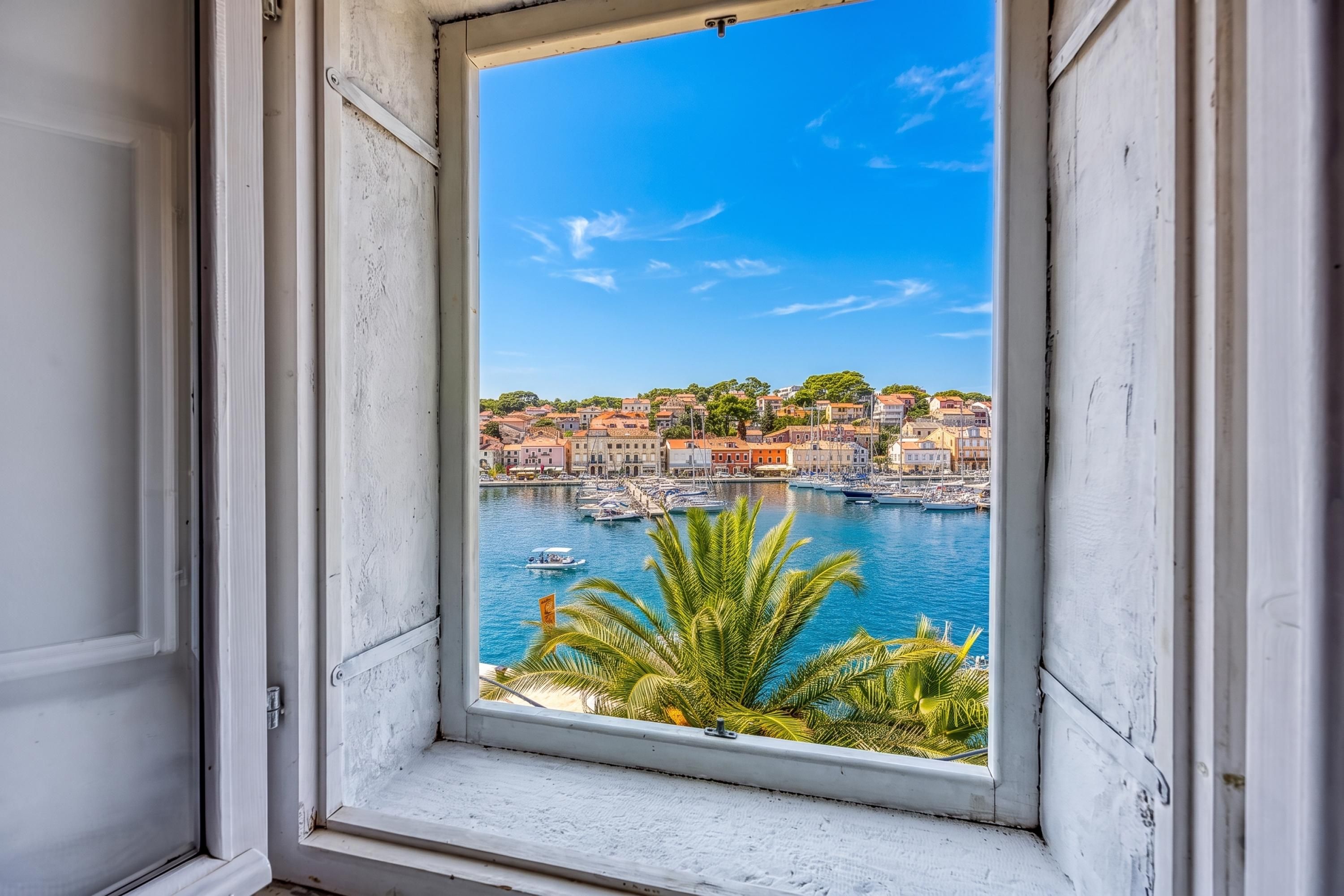 A window with a view of a coastal town, including buildings and boats.