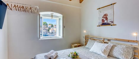 Une chambre avec un lit, une fenêtre donnant sur des immeubles et une marina, un plafond en bois et une œuvre d’art accrochée au mur.