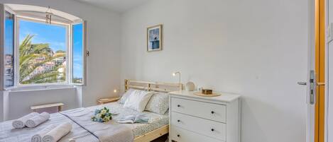 A bedroom with a bed, bedside tables, a nightstand, a dresser, a window with a view, and a framed picture on the wall.