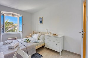 Une chambre à coucher comprenant un lit, des tables de chevet, une commode, une coiffeuse, une fenêtre avec vue et un tableau encadré accroché au mur.