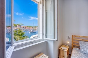Une chambre avec vue sur un port, une table de chevet en bois avec une lampe et un lit agrémenté d’un coussin à motifs.