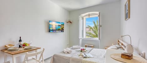 Un dormitorio con cama, escritorio, silla, ventana con vistas y un cuadro en la pared.