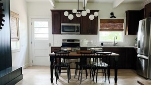 Una cocina amplia con piso de madera, gabinetes oscuros, una isla central con sillas, microondas empotrado, horno y refrigerador.