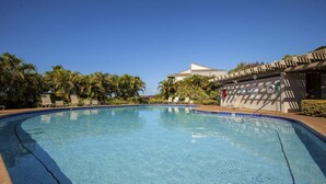 En klarblå swimmingpool med liggestole og palmer.