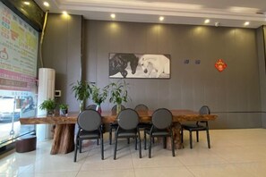 Un espace d’accueil comprenant un comptoir de réception en bois, quatre chaises, une plante en pot, un tableau accroché au mur et un objet décoratif rouge.