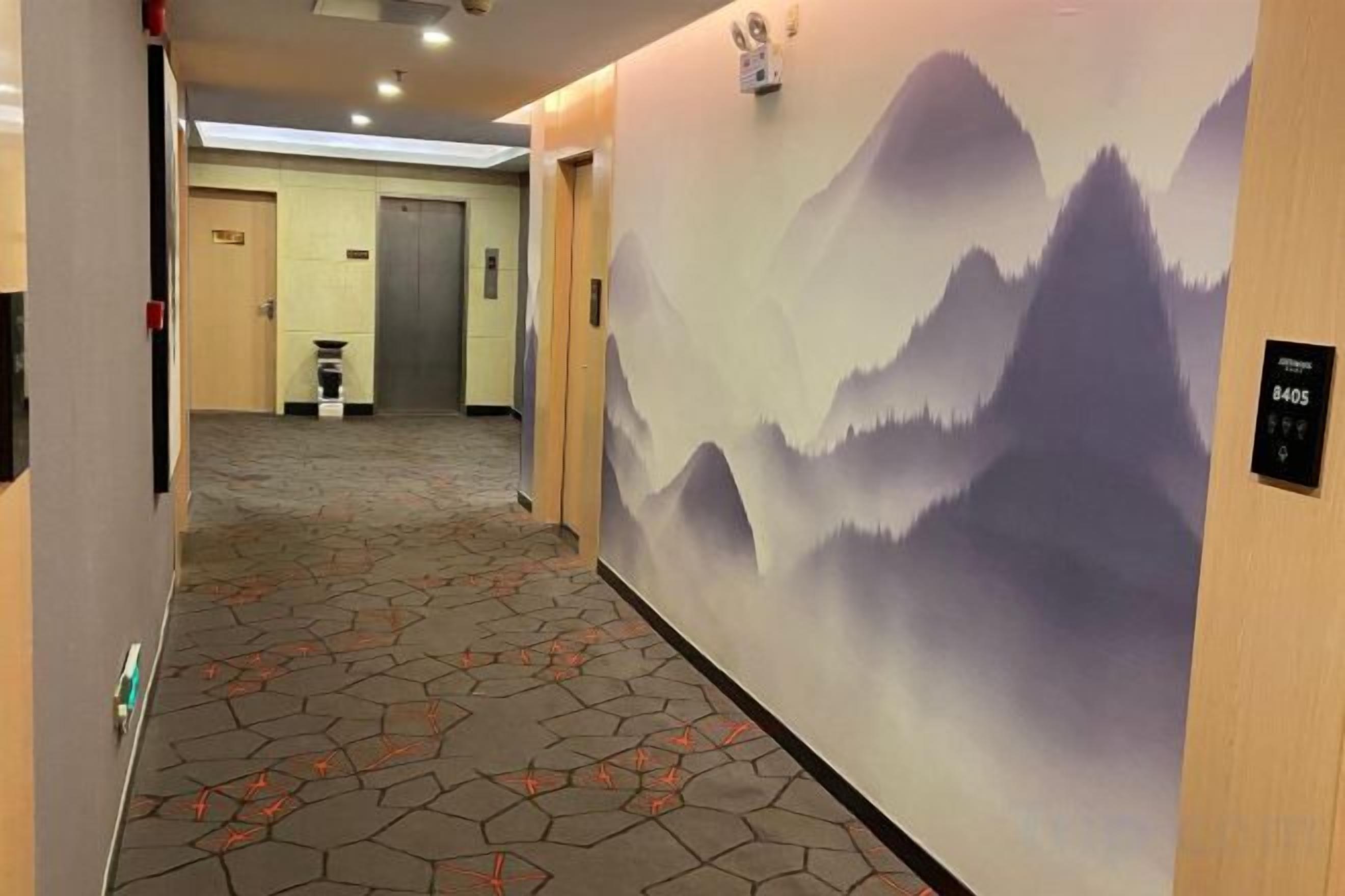A hotel corridor with a carpeted floor, a wall mural of mountains, and a door with a sign.