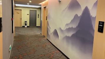 A hotel corridor with a carpeted floor, a wall mural of mountains, and a door with a sign.