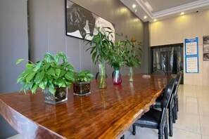 A conference table with chairs, surrounded by potted plants, in a room with a tiled floor and a framed picture on the wall. - Dongguan Haiyi Chain Hotel (Dongguan)