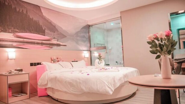 A modern bedroom with a round bed, a nightstand, a bedside table, a vase with flowers, and a wall-mounted mirror. - Dongguan Haiyi Chain Hotel (Dongguan)