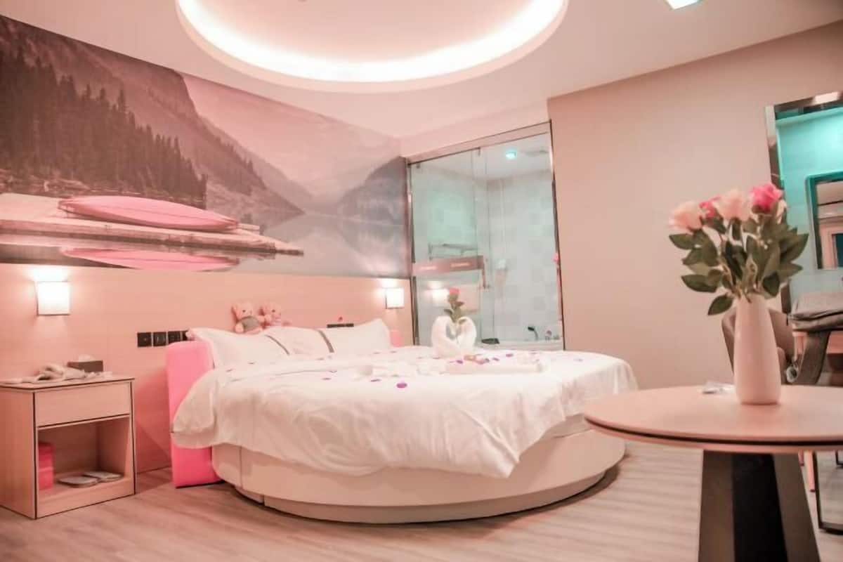 Quarto moderno com cama redonda, mesa de cabeceira, vaso com flores e espelho fixado na parede.