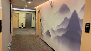 A hotel corridor with a patterned carpet, a wall mural of mountains, and an elevator with a sign indicating the floor number. - Dongguan Haiyi Chain Hotel (Dongguan)