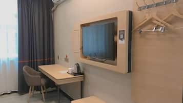 A hotel room with a desk, chair, television, and coat hooks.
