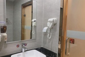 Une salle de bain équipée d’un lavabo, de deux sèche-cheveux fixés au mur, d’un miroir et d’une porte dotée d’une poignée à tirer.