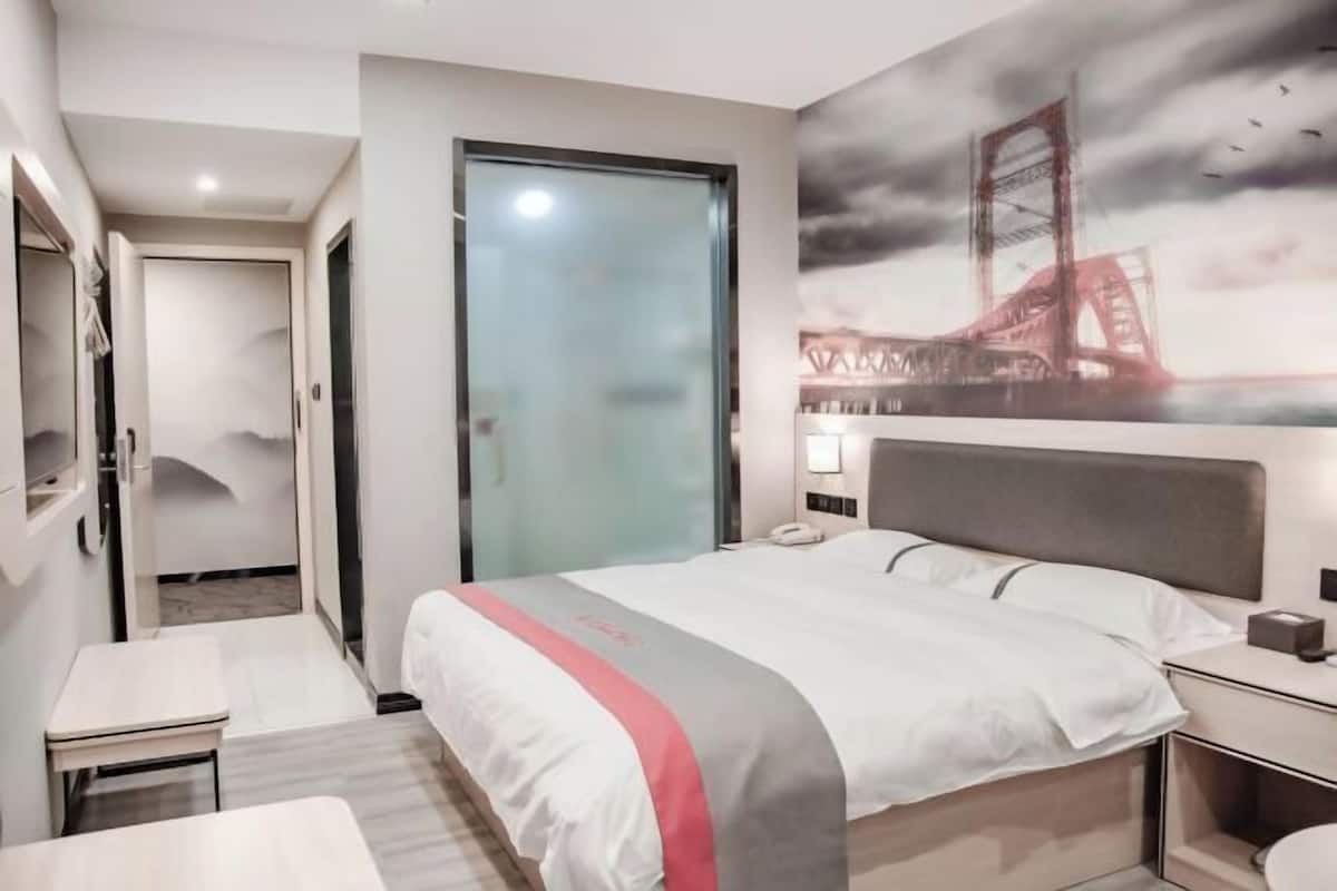 Quarto de hotel com cama, mesa de cabeceira e uma grande janela com vista para uma ponte.
