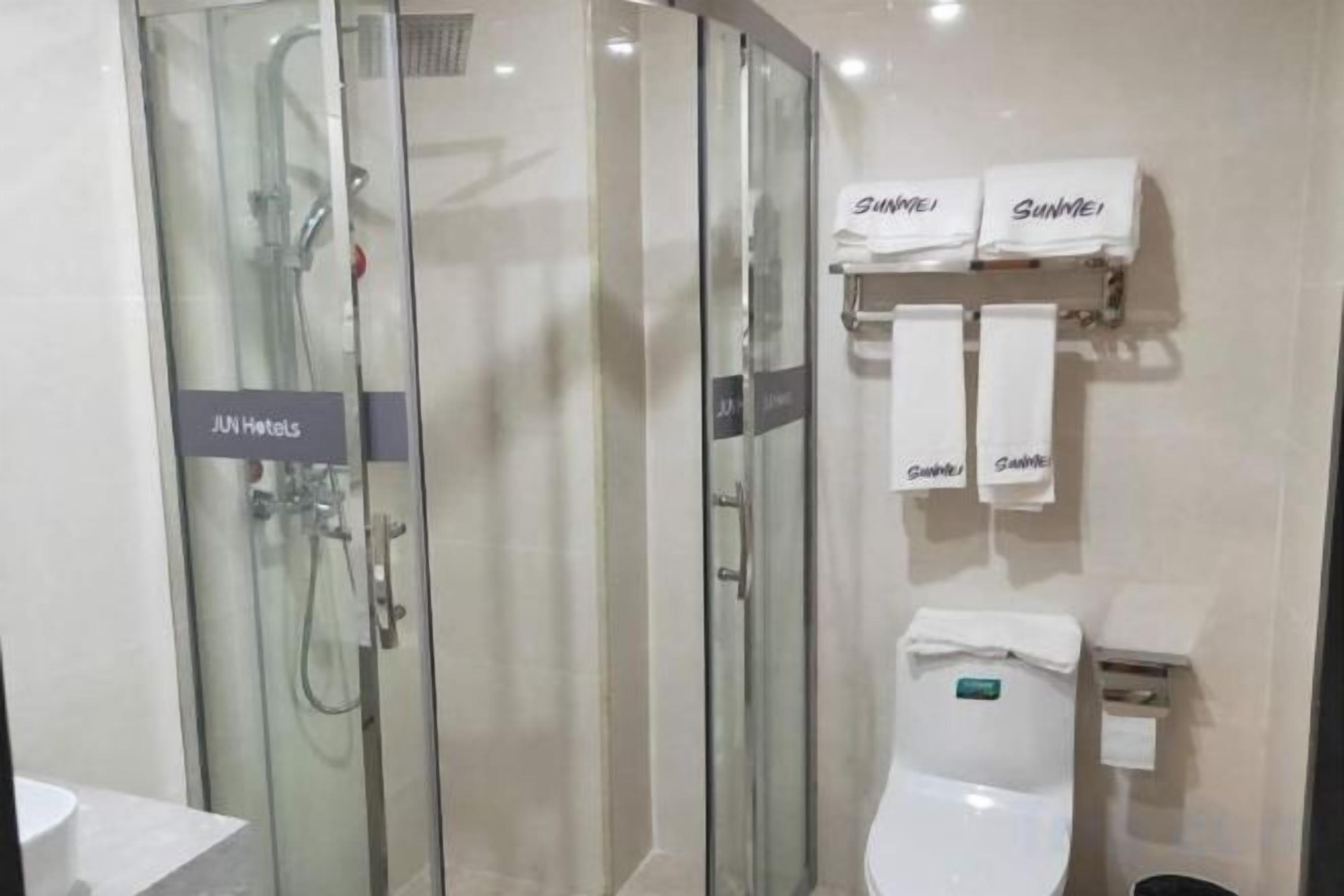 A bathroom with a glass-enclosed shower, a toilet, and two towels hanging on a rack.
