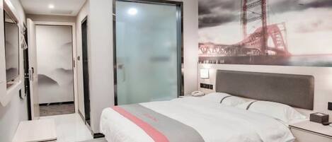 A hotel room with a bed, bedside table, and a painting of a bridge.
