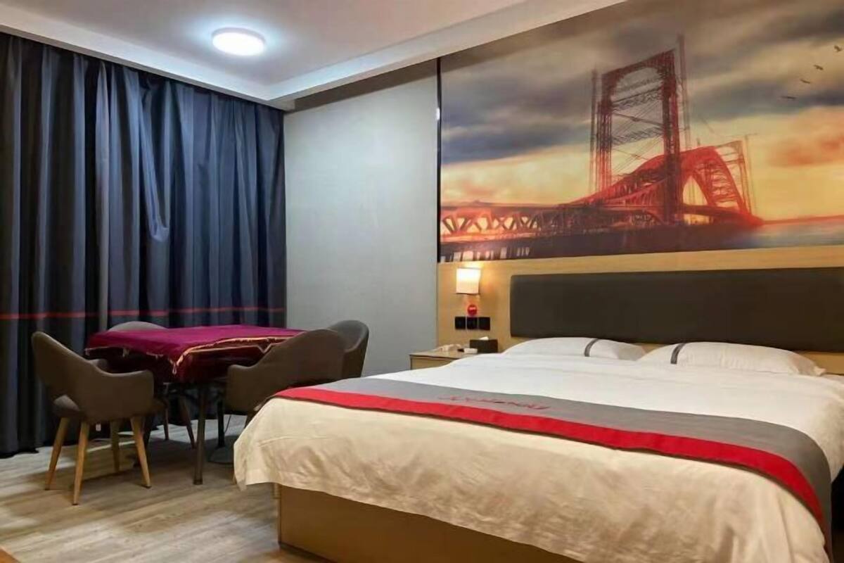 Quarto de hotel com uma cama, uma escrivaninha, duas cadeiras, um quadro grande de uma ponte e uma janela com cortinas.