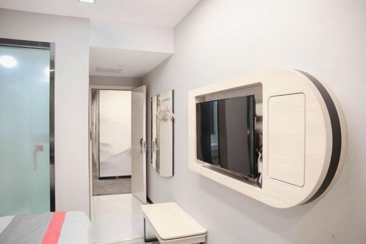 Une chambre d’hôtel moderne, équipée d’un lit, d’une petite table de chevet, d’un téléviseur fixé au mur et d’une porte donnant sur une autre pièce.