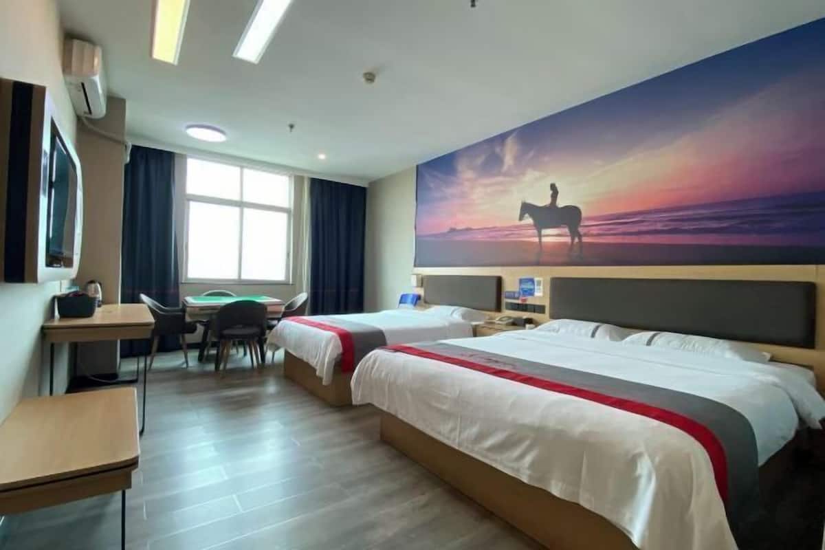 Quarto de hotel com duas camas, uma escrivaninha, uma cadeira, uma televisão e um quadro grande representando o pôr do sol.