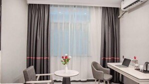 A modern hotel room with a desk, two chairs, a small table with a vase of flowers, and a large window with curtains. - Dongguan Haiyi Chain Hotel (Dongguan)