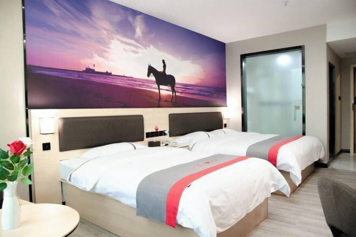 Quarto de hotel com duas camas, um grande mural na parede, um vaso com uma flor e uma porta de vidro.