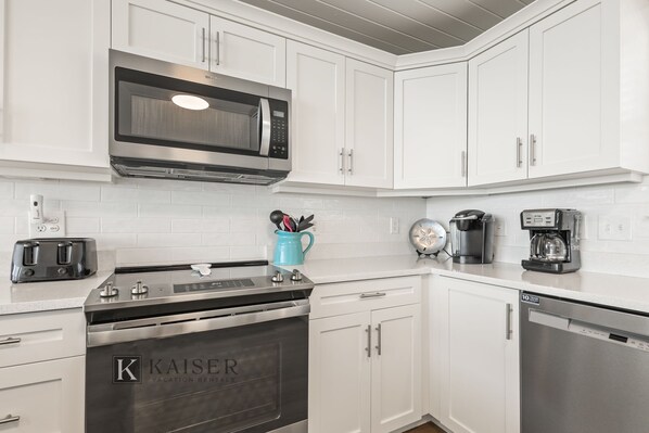 A modern kitchen with white cabinetry, a stainless steel microwave, a toaster, a coffee maker, and a dishwasher.