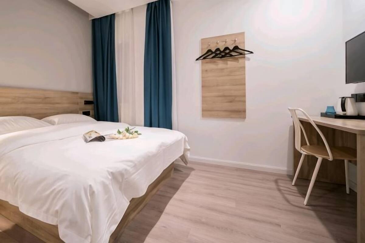 A hotel room with a bed, a desk, a chair, a TV, and a coat rack.