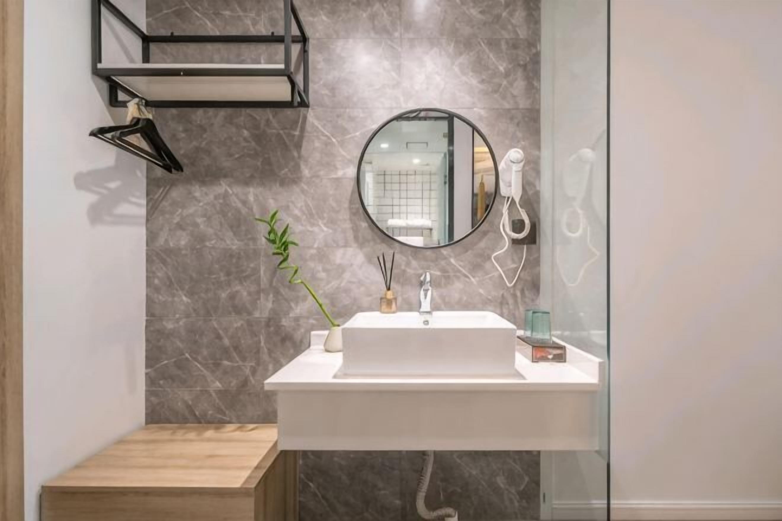 Un baño con un lavabo blanco, un espejo redondo, un toallero colgante y una planta.