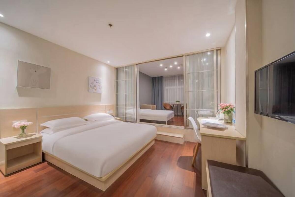 A hotel room with a large bed, a desk, a chair, a TV, and a mirror.