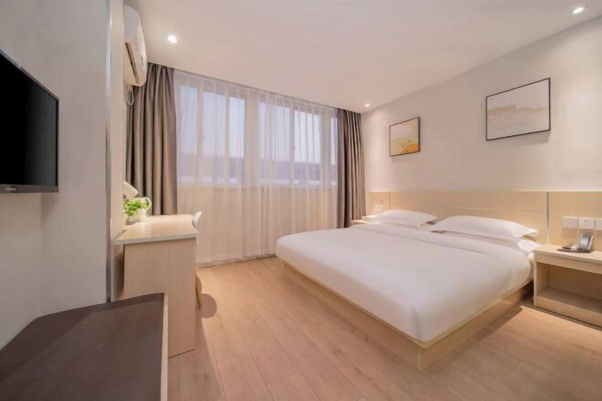 A modern hotel room with a large bed, a flat-screen TV, a desk, and a window with curtains.