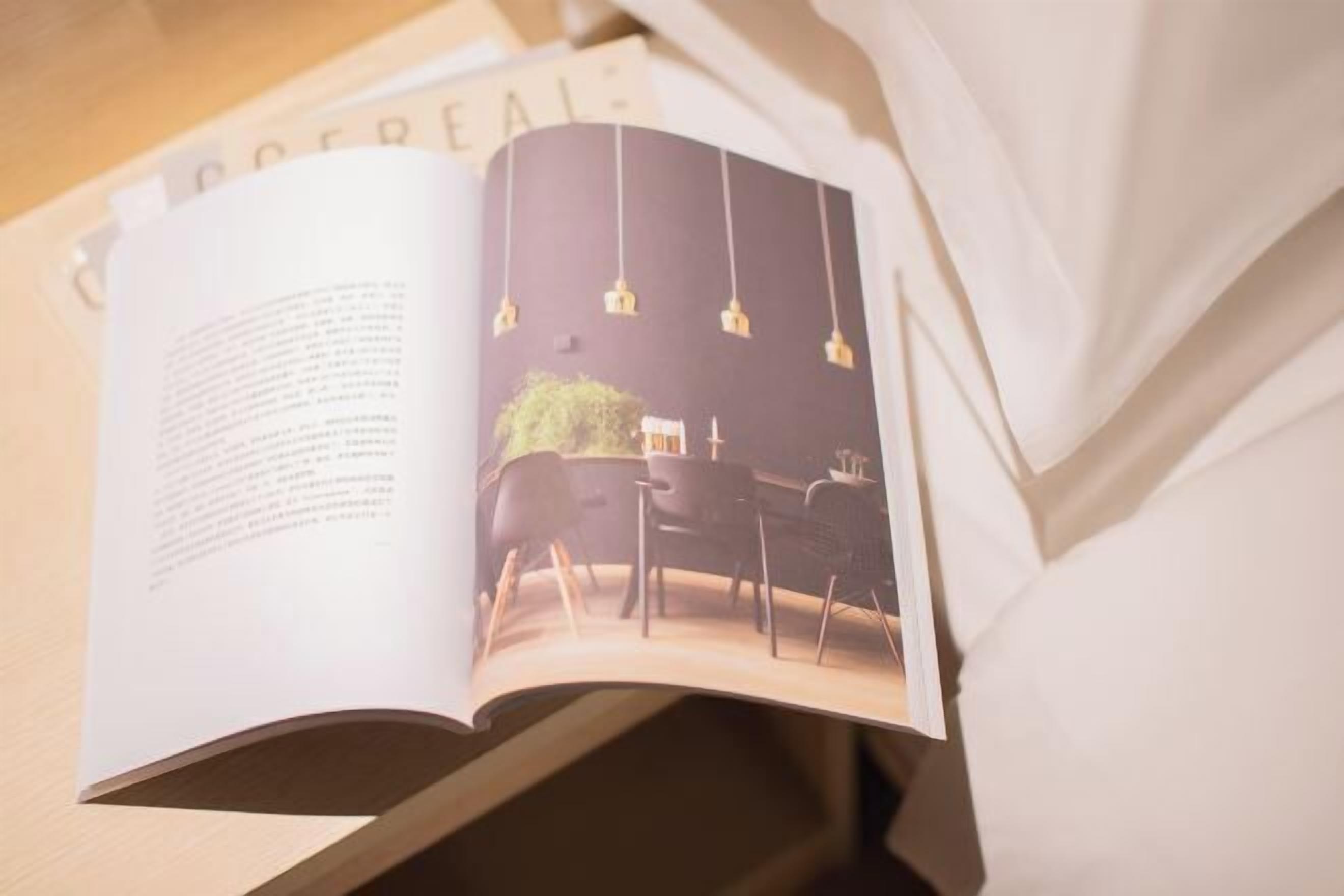 Una revista abierta con una página que muestra un diseño de interiores moderno, incluyendo una zona de comedor con lámparas colgantes y una mesa.