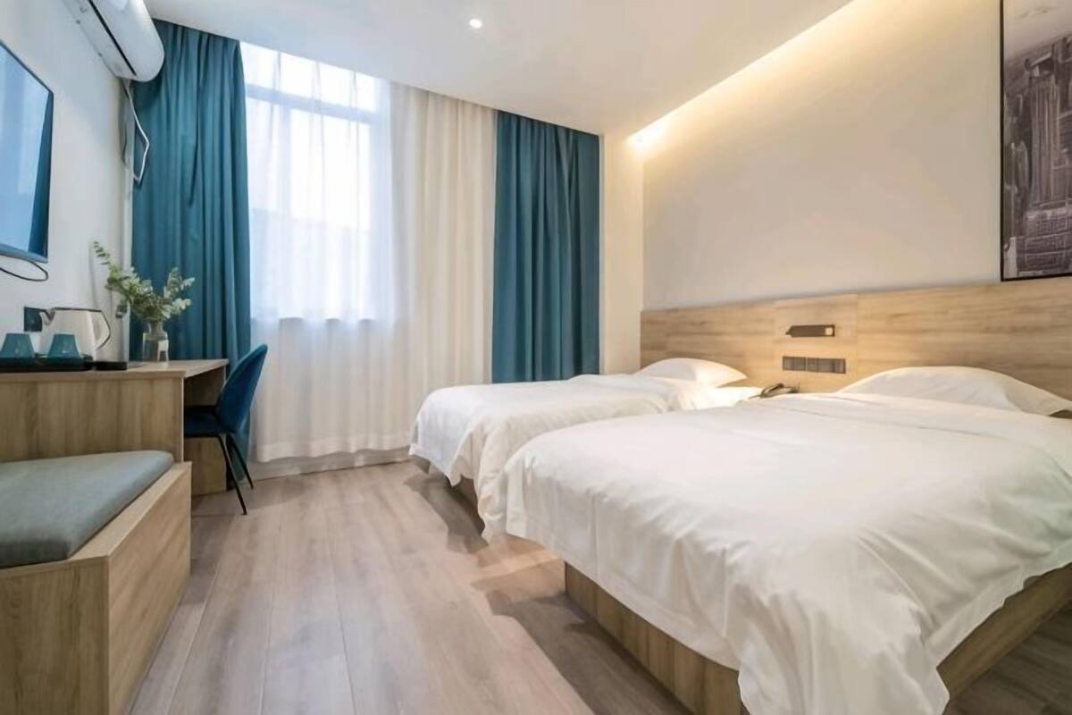 A hotel room with two beds, a desk, a chair, and a window with curtains.