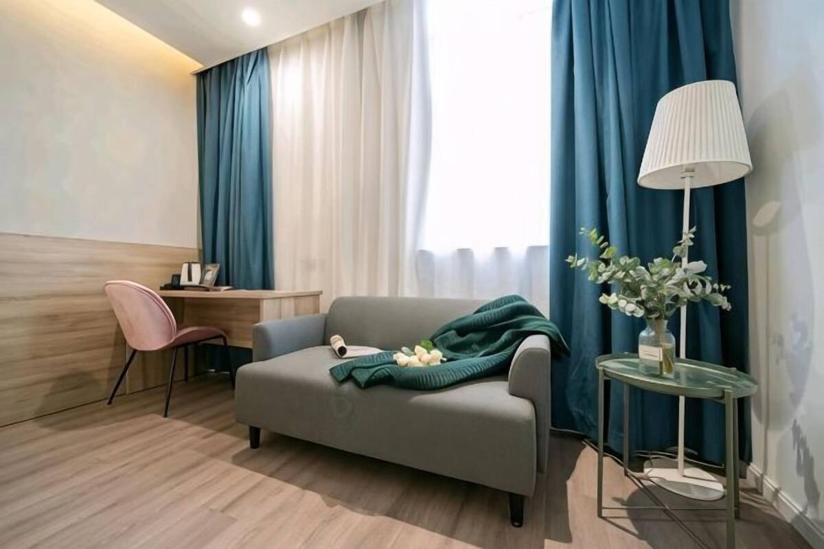 A modern hotel room with a sofa, a small table with a lamp, a chair, and a desk.