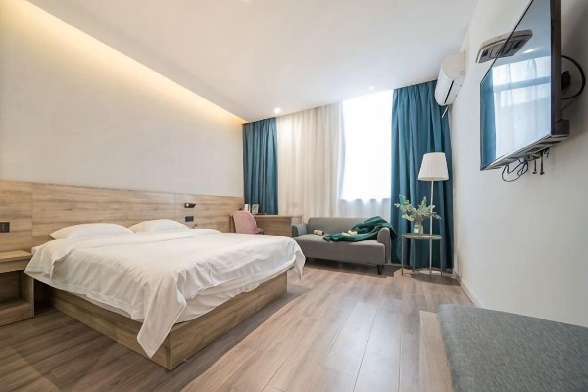 Habitación de hotel con cama, sofá, televisor y ventana con cortinas.