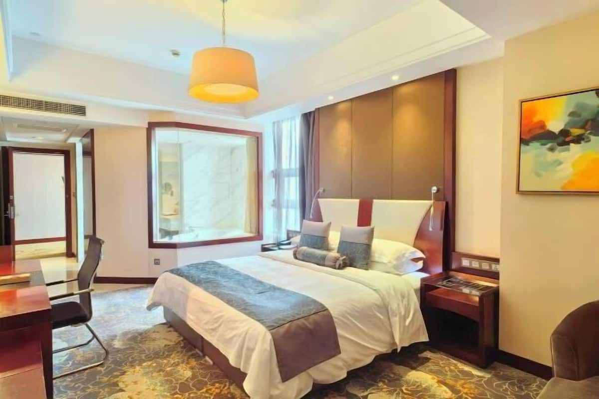 A hotel room with a large bed, a desk, a chair, a nightstand, and a painting on the wall.