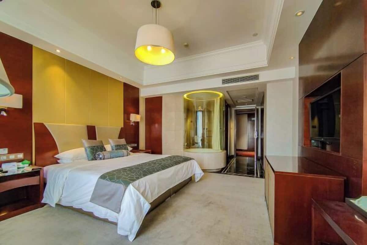 A hotel room with a large bed, a bedside table, a mirror, a TV, and a glass partition.