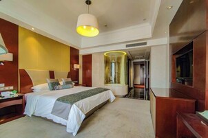 Habitación de hotel con una cama grande, una mesita de noche, un espejo, un televisor y un panel de vidrio.